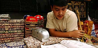 Tradition und Moderne: Ein junger Uigure lernt an seinem Verkaufstand für Seidenstoffe und traditionelle Kopfbedeckungen Englisch